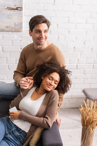 Sonriente Hombre Cogido Mano Novia Afroamericana Con Teléfono Celular Sofá — Foto de Stock