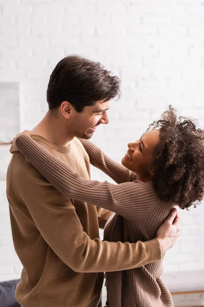 Alegre Interracial Casal Olhando Para Outro Enquanto Abraçando Casa — Fotografia de Stock