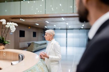Otel resepsiyonunda son sınıf iş kadını ve bulanık ön planda iki ırklı koruma.