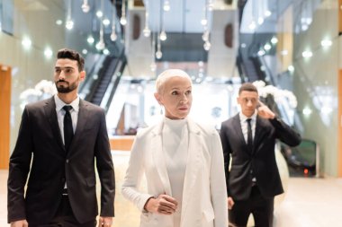 Lüks otel lobisinde çok ırklı korumaların yanında üst düzey bir iş kadını.
