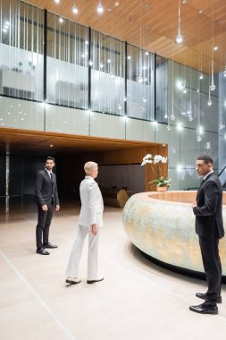 Otel resepsiyonuna doğru yürüyen kıdemli iş kadınının yanında çok ırklı korumalar
