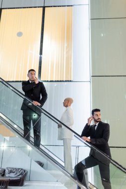 Otelin yürüyen merdiveninde özel korumaların yanında zengin bir iş kadını.