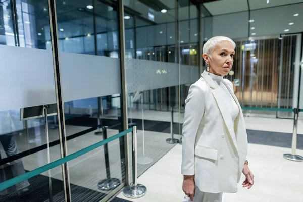 身穿白色西服的高级商务女士站在现代宾馆入口附近 — 图库照片