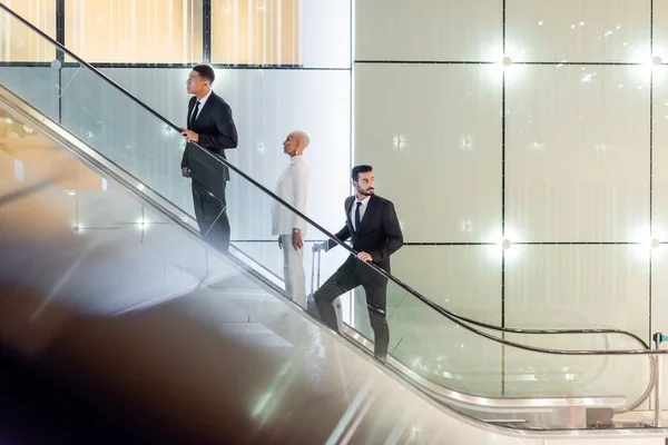 Ώριμη Επιχειρηματίας Στις Κυλιόμενες Σκάλες Του Ξενοδοχείου Κοντά Διαφυλετικούς Σωματοφύλακες — Φωτογραφία Αρχείου