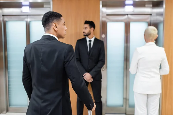 business lady waiting for elevator in hotel near private interracial bodyguards