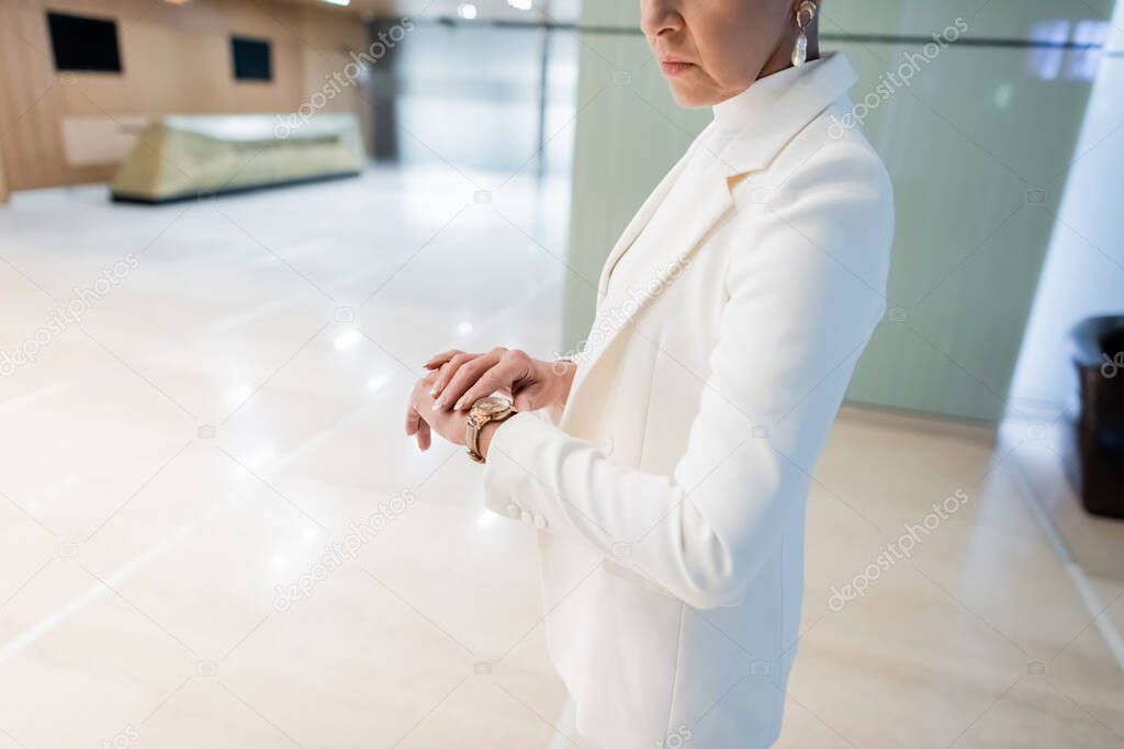 cropped view of wealthy businesswoman checking time on golden wristwatch in hotel lobby