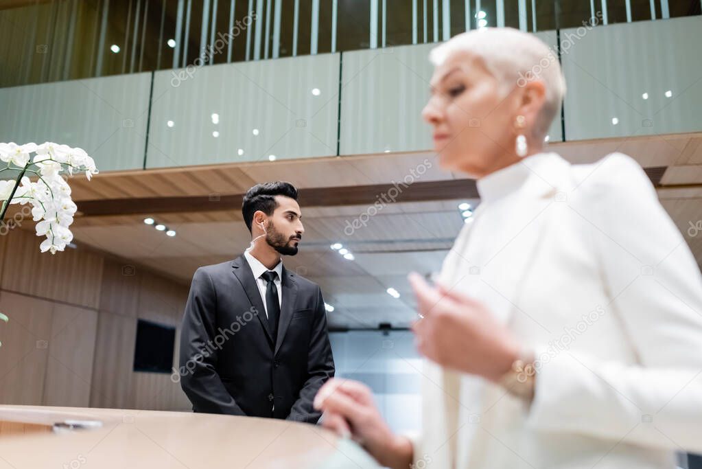 bi-racial bodyguard looking away while blurred business lady checking in at hotel reception