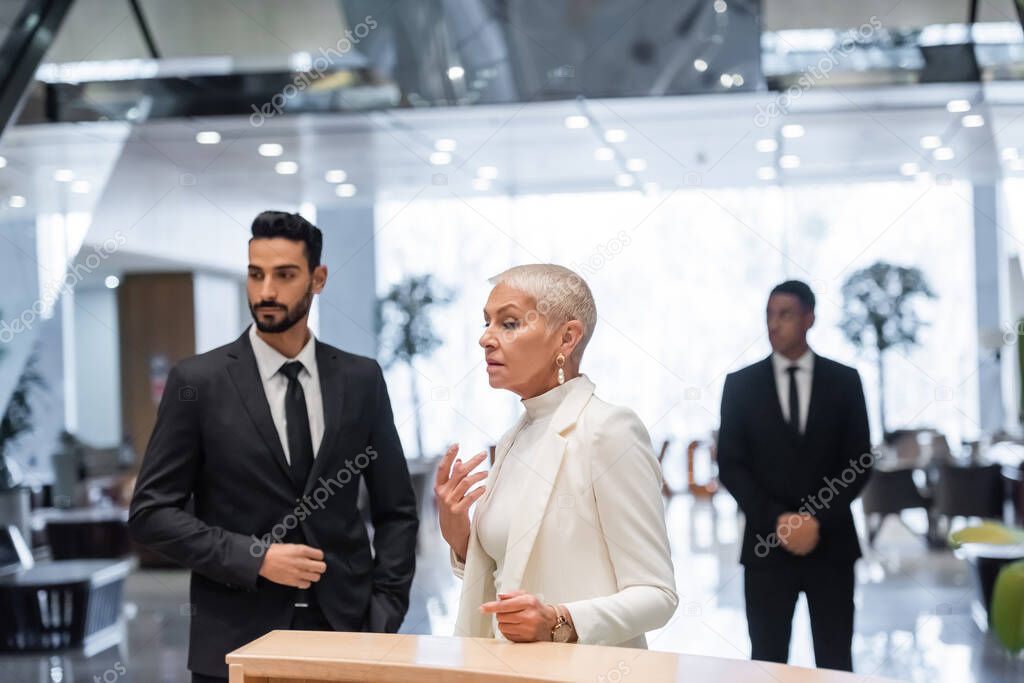 interracial bodyguards protecting mature businesswoman standing at hotel reception