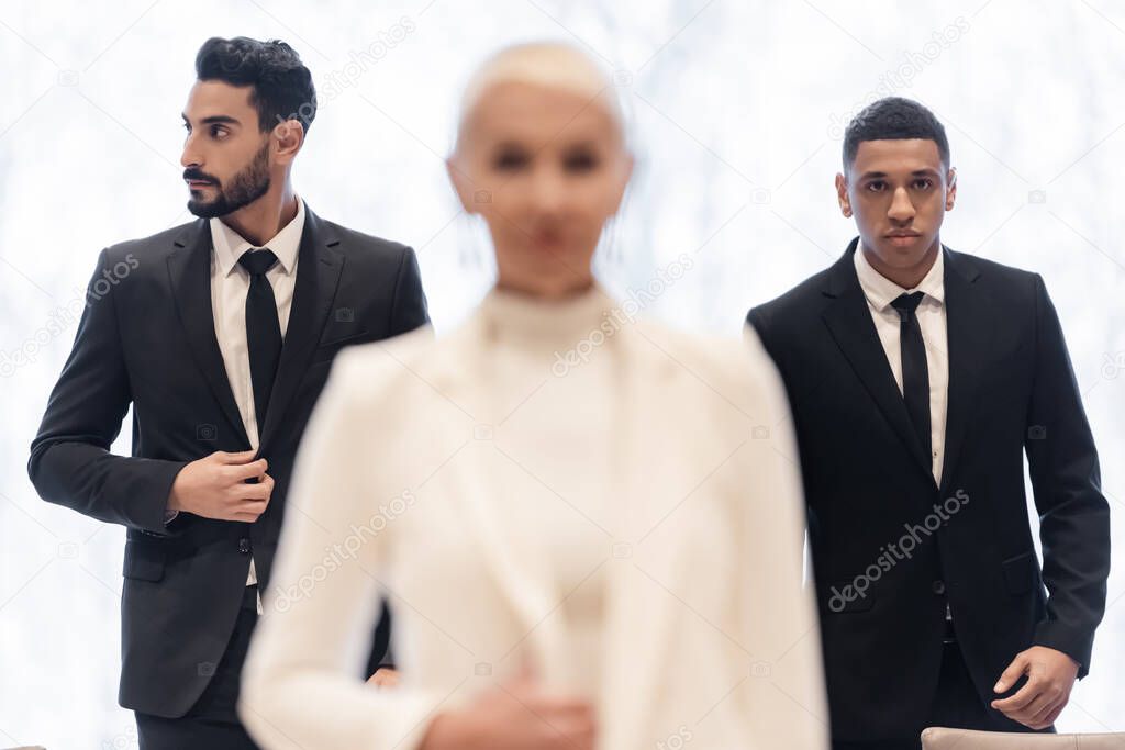 interracial bodyguards in formal wear escorting blurred businesswoman during business trip
