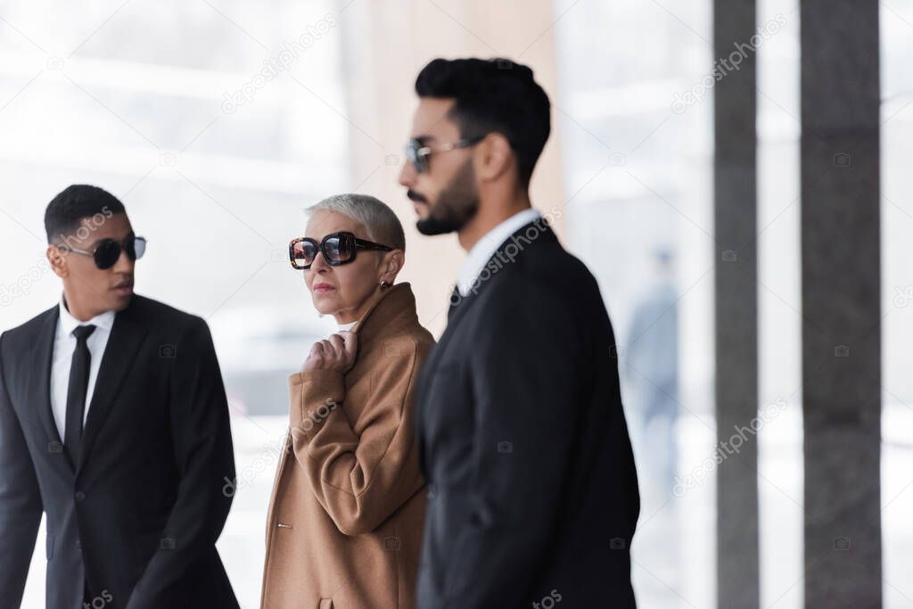 blurred multiethnic bodyguards escorting stylish senior businesswoman in city