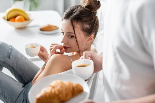 Mujer Joven Sosteniendo Taza Mirando Hombre Borroso Con Croissant Plato — Foto de Stock