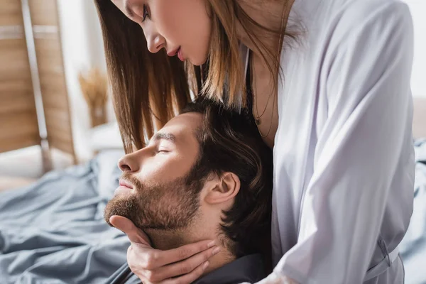 young woman in silk robe hugging bearded boyfriend with closed eyes