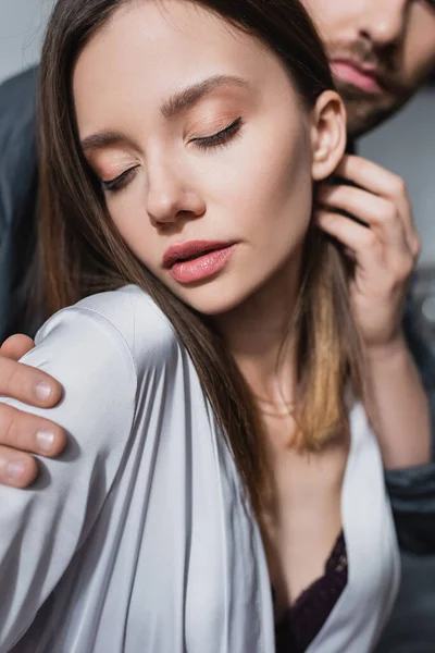 sensual woman in silk robe adjusting hair near blurred man