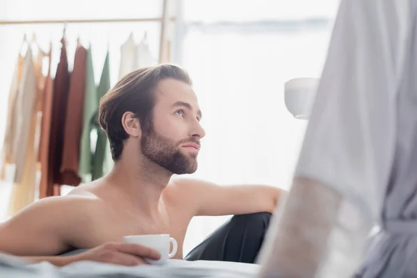 bearded man looking at woman in robe and holding cup