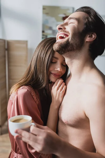 幸せな男笑いの近くの彼女でピンクシルクのローブと保持カップのコーヒー — ストック写真