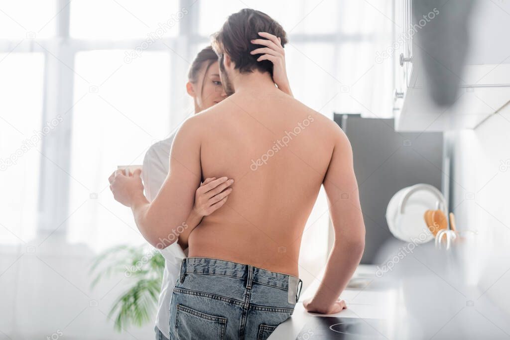 back view of shirtless man holding cup and hugging with sensual woman 