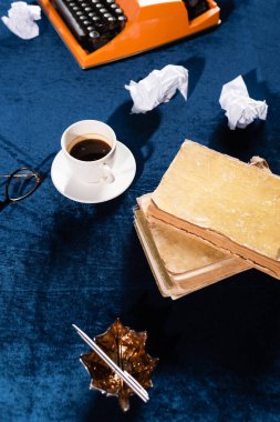 Kahve fincanı, klasik kitaplar, buruşuk kağıt ve mavi kadife masa örtüsü üzerinde klasik daktilo.