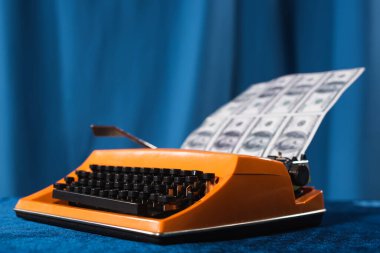 vintage typewriter and blurred dollar banknotes on blue background clipart