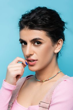 Düşünceli esmer kadın, mavi ışıkta el ele tutuşurken kameraya bakıyor.