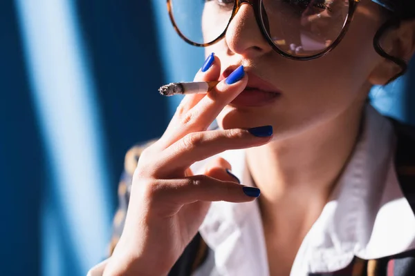 cropped view of vintage style woman with blue manicure smoking on blurred background