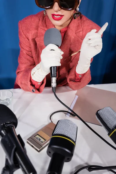 cropped view of vintage style woman pointing with finger during interview on blue background