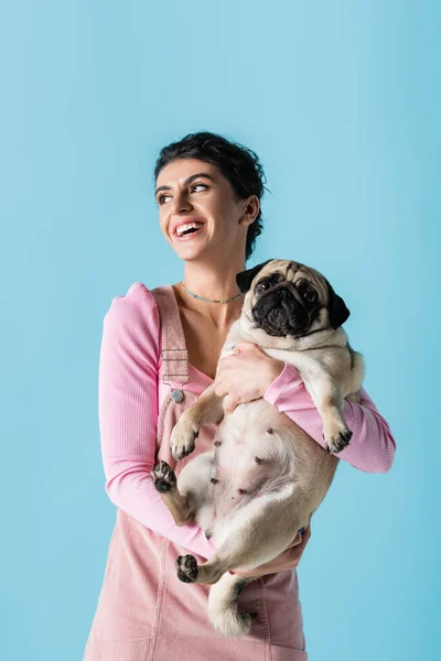 Glimlachende Vrouw Kijken Weg Houden Pug Hond Geïsoleerd Blauw — Stockfoto