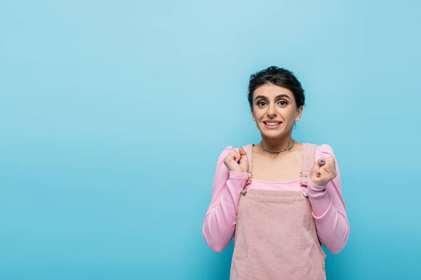 excited woman holding clenched fists for luck isolated on blue