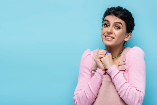 smiling woman showing please gesture while looking at camera isolated on blue