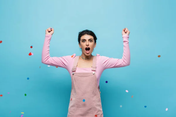 Overjoyed Woman Screaming Showing Win Gesture Falling Confetti Blue Background — Stock Photo, Image