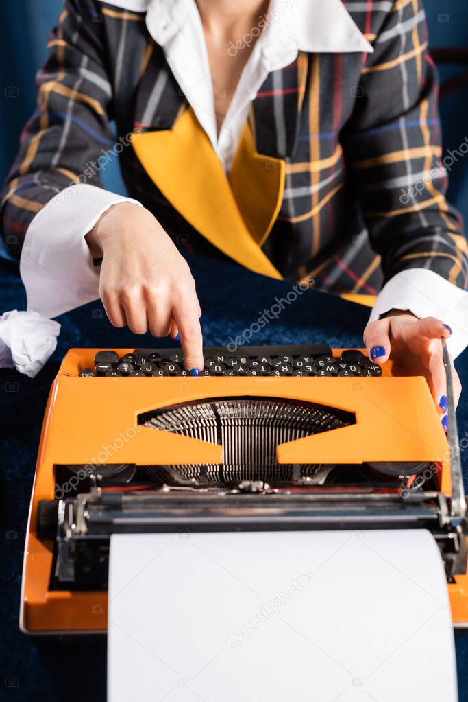 cropped view of newswoman in stylish blazer typing on vintage typewriter 