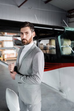 Takım elbiseli kendine güvenen iş adamı modern helikopterin yanındaki kameraya bakıyor.