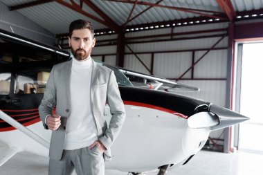Takım elbiseli kendine güvenen sakallı iş adamı modern helikopterin yanında el ele duruyor.