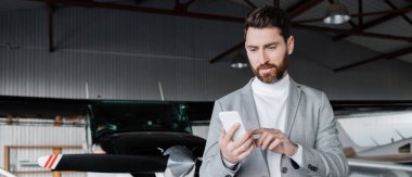 Sakallı adam modern helikopterin yanında akıllı telefon kullanıyor.
