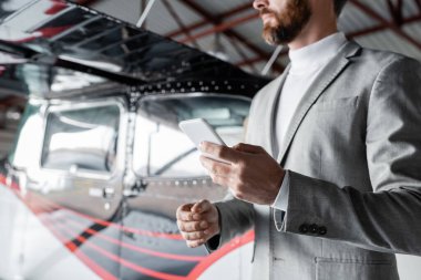 Resmi kıyafetli sakallı adamın modern helikopterin yanında cep telefonu taşıması