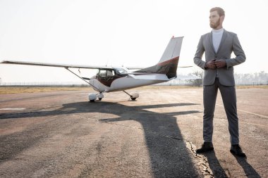 full length of bearded businessman in suit standing near helicopter outdoors  clipart