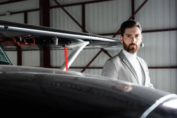 Γενειοφόρος Επιχειρηματίας Κοστούμι Κοιτάζοντας Κάμερα Κοντά Ελικόπτερο Στο Πάρκινγκ — Φωτογραφία Αρχείου