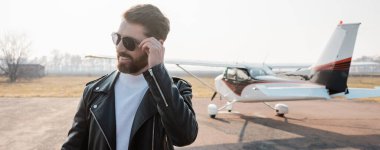 Havalı deri ceketli, helikopter ve pankartın yanında güneş gözlüğü takan memnun pilot.