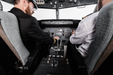 bearded pilot in cap using thrust lever near co-pilot in airplane simulator  clipart