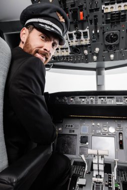 ... şapkalı sakallı pilot gülümsüyor ve uçak simülatöründe kameraya bakıyor. 