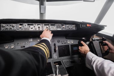 cropped view of pilot reaching control panel near co-pilot using yoke in airplane simulator  clipart