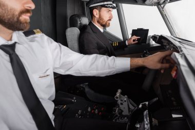 Kaptan, uçak simülatöründe yardımcı pilotun yanında boş ekranlı bir cihaz kullanıyor.