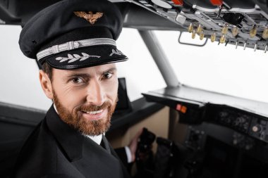 Şapkalı neşeli pilot uçak simülatöründeki kameraya bakıyor. 