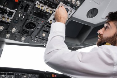 Sakallı pilot, uçak simülatörünün tepe düğmesine basıyor.