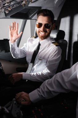 Güneş gözlüklü neşeli pilot uçakta yardımcı pilotun yanında el sallıyor. 