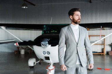 Gri takım elbiseli sakallı adam modern helikopterin yanında duruyor. 