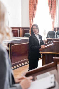 brunette witness looking at blurred prosecutor during litigation in court clipart