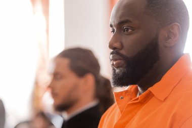selective focus of accused african man near blurred bailiff in courtroom clipart