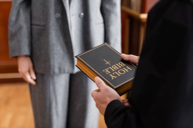 partial view of bailiff holding holy bible near woman in court clipart