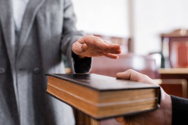 partial view of woman giving oath on holy bible in courtroom clipart