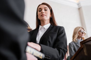 low angle view of brunette witness giving oath on bible in court clipart